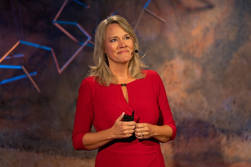 A female presenter looking toward the audience with a smile