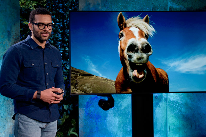 A male presenter with hands clasped, beside a screen displaying an image of a smiling horse